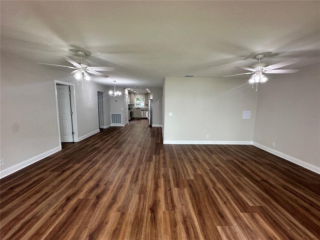 An open-concept living area features wood-look flooring, two ceiling fans, and a view toward the kitchen — 100 EL CAMINO DR UNIT 104, WINTER HAVEN, FL