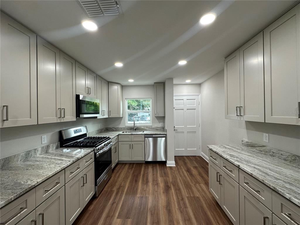 A kitchen features light gray cabinets, granite countertops, stainless steel appliances, and wood-look flooring — 100 EL CAMINO DR UNIT 104, WINTER HAVEN, FL