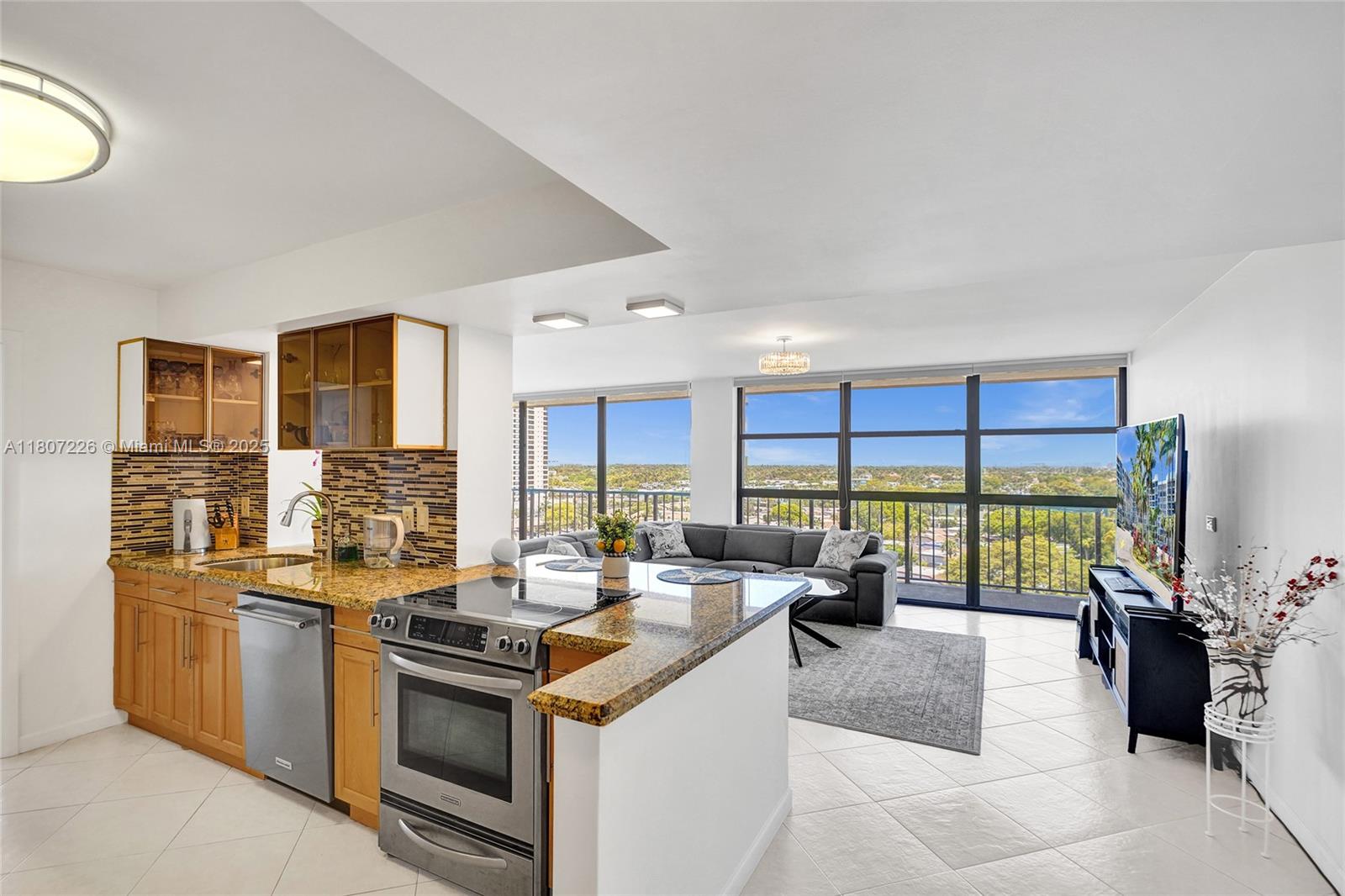 An open-concept kitchen with granite countertops and stainless steel appliances overlooks a living area — 200 Leslie Dr # 1031, Hallandale Beach FL 33009, HALLANDALE BEACH, FL