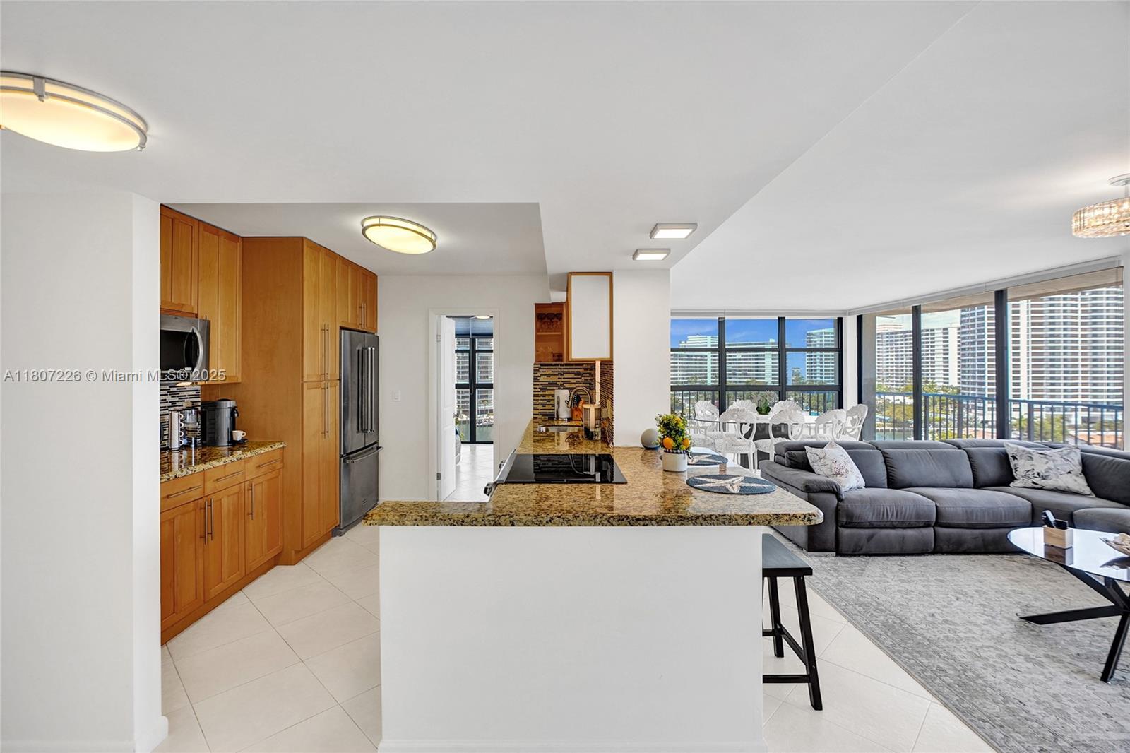 A kitchen with wood cabinets and granite countertops opens into a living area with views — 200 Leslie Dr # 1031, Hallandale Beach FL 33009, HALLANDALE BEACH, FL