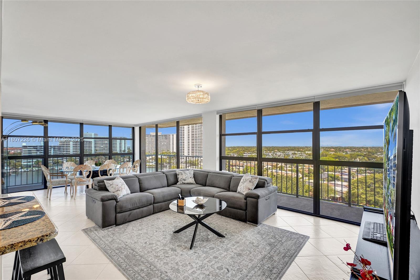 A living room with a gray sectional sofa, glass coffee table, and floor-to-ceiling windows — 200 Leslie Dr # 1031, Hallandale Beach FL 33009, HALLANDALE BEACH, FL