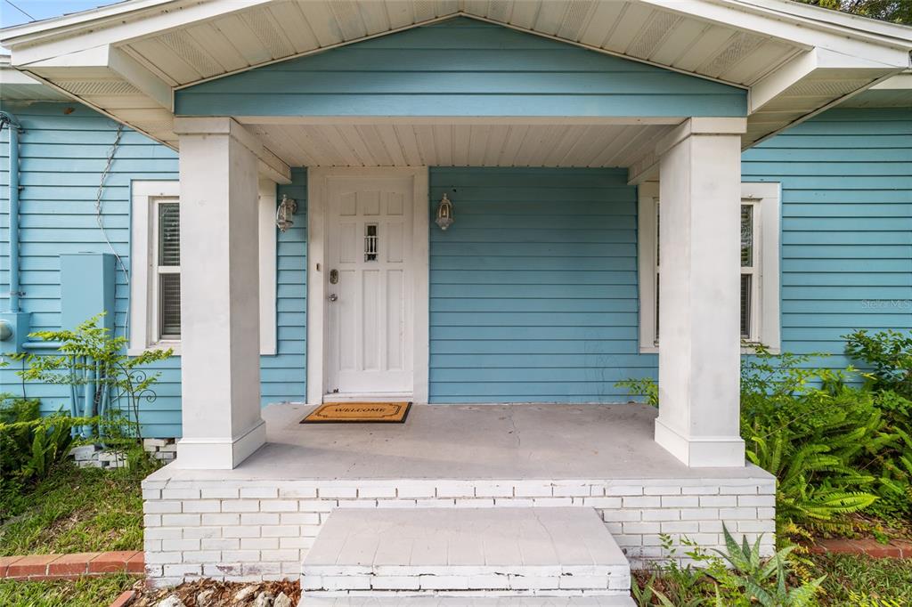 A blue house exterior features a covered front porch with white columns and a door — 20837 WALNUT STREET, DUNNELLON, FL