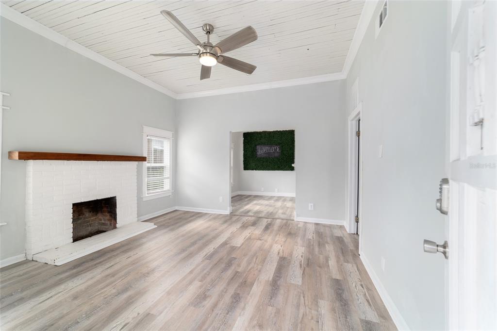 A living room with a white brick fireplace, wood-look flooring, and a white plank ceiling — 20837 WALNUT STREET, DUNNELLON, FL