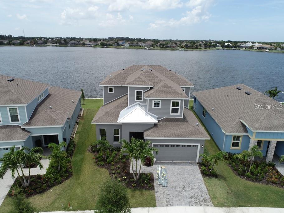 An aerial view shows a gray two-story house situated between two blue houses by a lake — 5327 WISHING ARCH DRIVE, APOLLO BEACH, FL