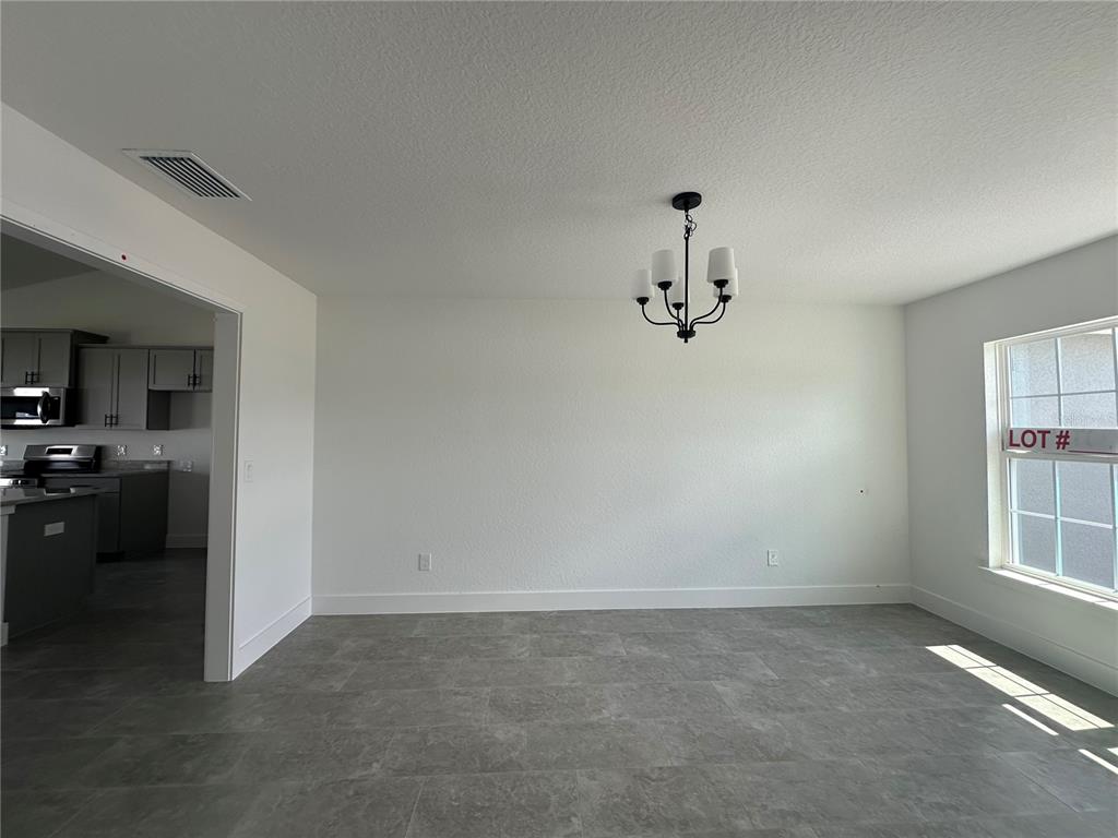 A dining area with gray tile flooring, a chandelier, and a view into the kitchen — 12605 NE 48TH STREET, OXFORD, FL