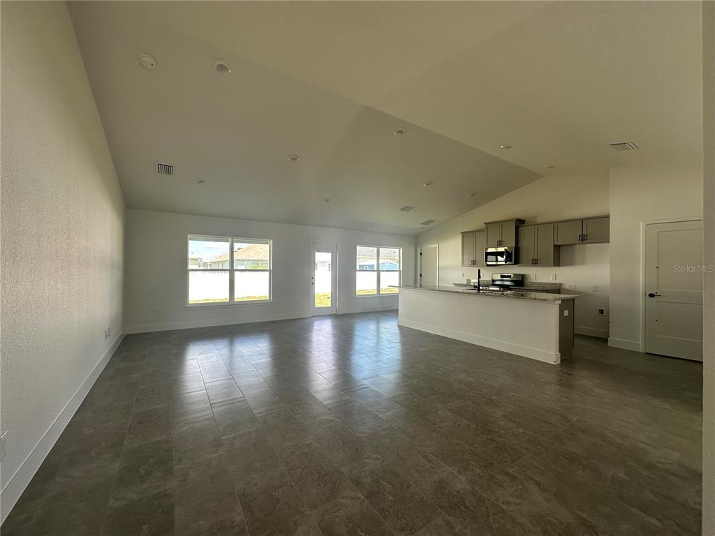 An open-concept living area features tile flooring, a vaulted ceiling, and a kitchen with cabinets — 12605 NE 48TH STREET, OXFORD, FL