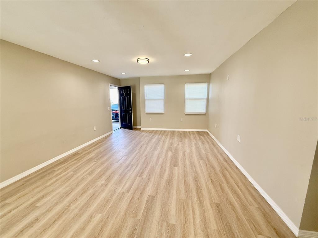 An empty living room features light wood-look flooring, beige walls, recessed lighting, and a dark door — 2769 L B MCLEOD ROAD UNIT 2769A, ORLANDO, FL