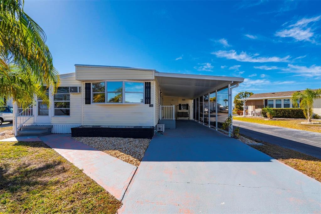 A light-colored mobile home features a concrete driveway, a carport, and a small front yard — 1000 KINGS HIGHWAY UNIT 132, PORT CHARLOTTE, FL