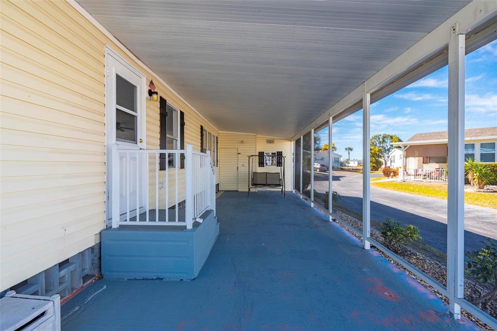 A covered outdoor porch with a blue floor, white railing, and a small swing — 1000 KINGS HIGHWAY UNIT 132, PORT CHARLOTTE, FL