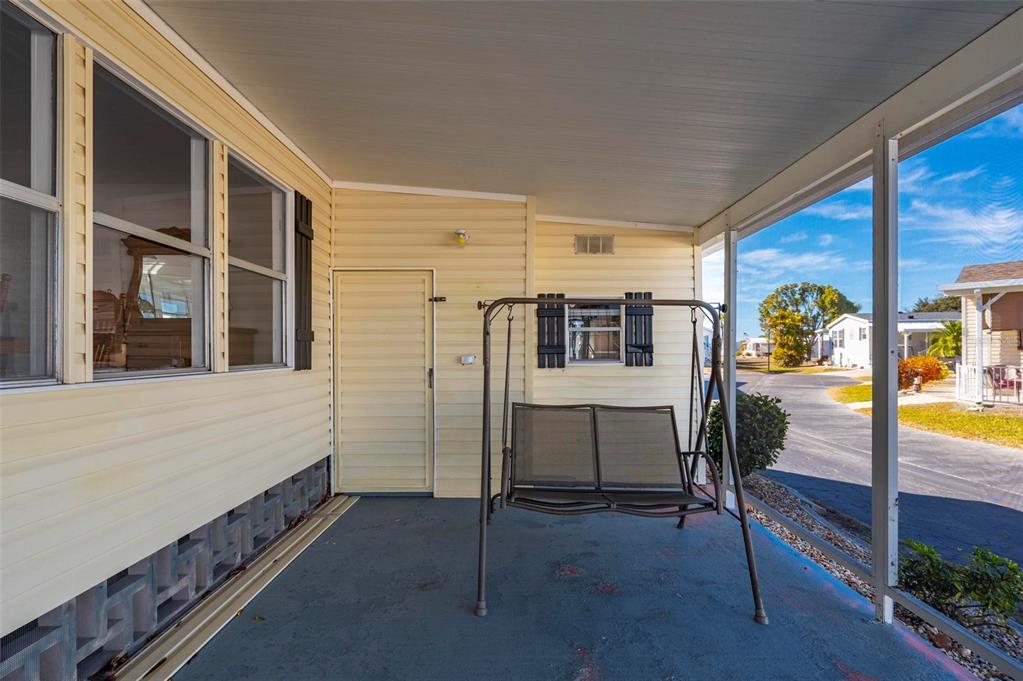 A covered porch with light yellow siding, a metal swing, and a view of the street — 1000 KINGS HIGHWAY UNIT 132, PORT CHARLOTTE, FL
