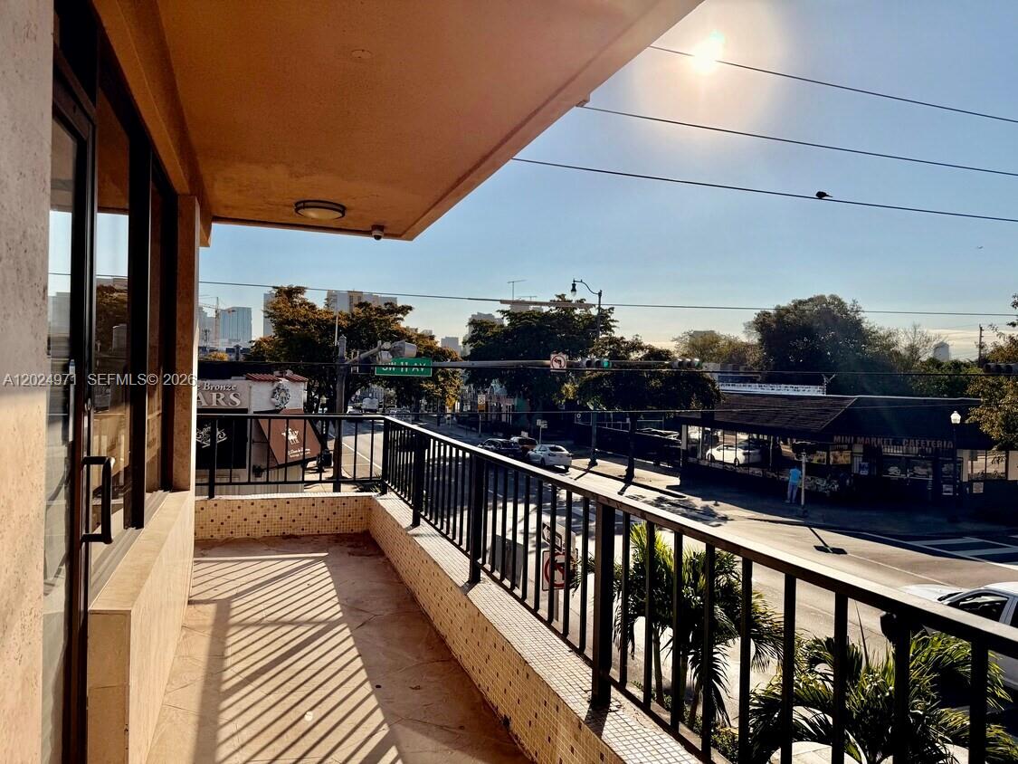 A balcony with a metal railing overlooks a street intersection with a small market — 1101 SW 8th St # 203, Miami FL 33130, MIAMI, FL