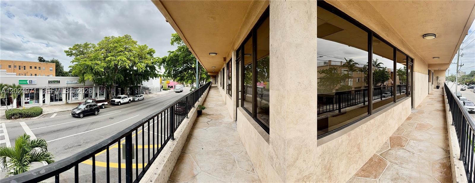 A stone-tiled outdoor balcony with a black metal railing overlooks a street and nearby buildings — 1101 SW 8th St # 203, Miami FL 33130, MIAMI, FL