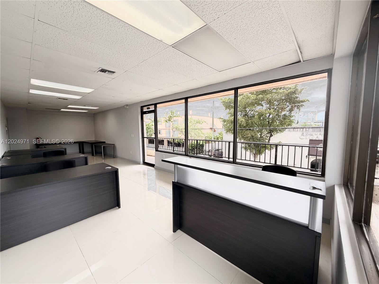 An office space features dark desks, white tile flooring, and large windows overlooking a balcony — 1101 SW 8th St # 203, Miami FL 33130, MIAMI, FL
