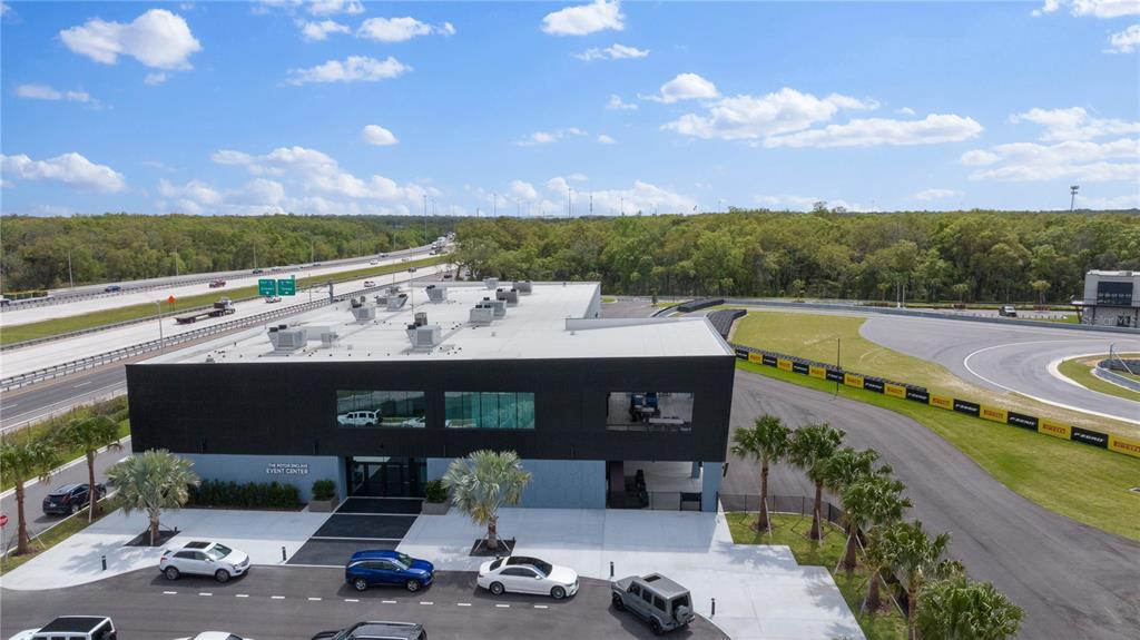 An aerial view shows a modern black event center building next to a paved racetrack — 6500 MOTOR ENCLAVE WAY UNIT 506, TAMPA, FL