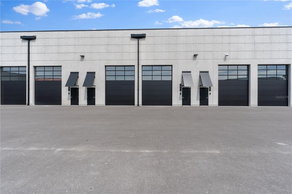 The exterior of a modern industrial building features multiple roll-up doors and pedestrian entrances — 6500 MOTOR ENCLAVE WAY UNIT 506, TAMPA, FL