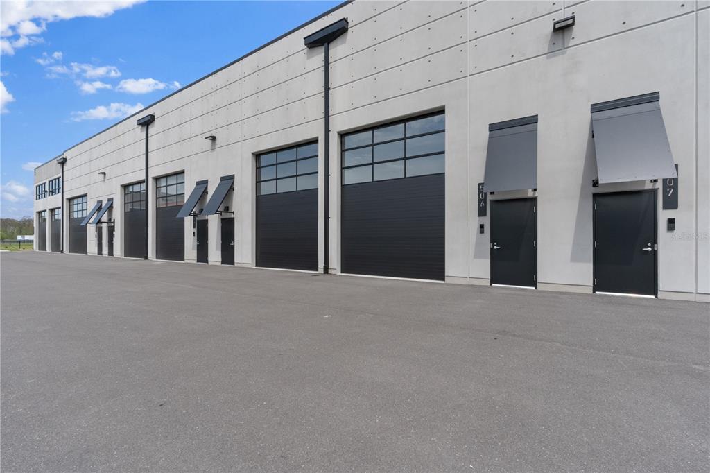 The exterior of a modern industrial building features multiple black roll-up doors and entry doors — 6500 MOTOR ENCLAVE WAY UNIT 506, TAMPA, FL