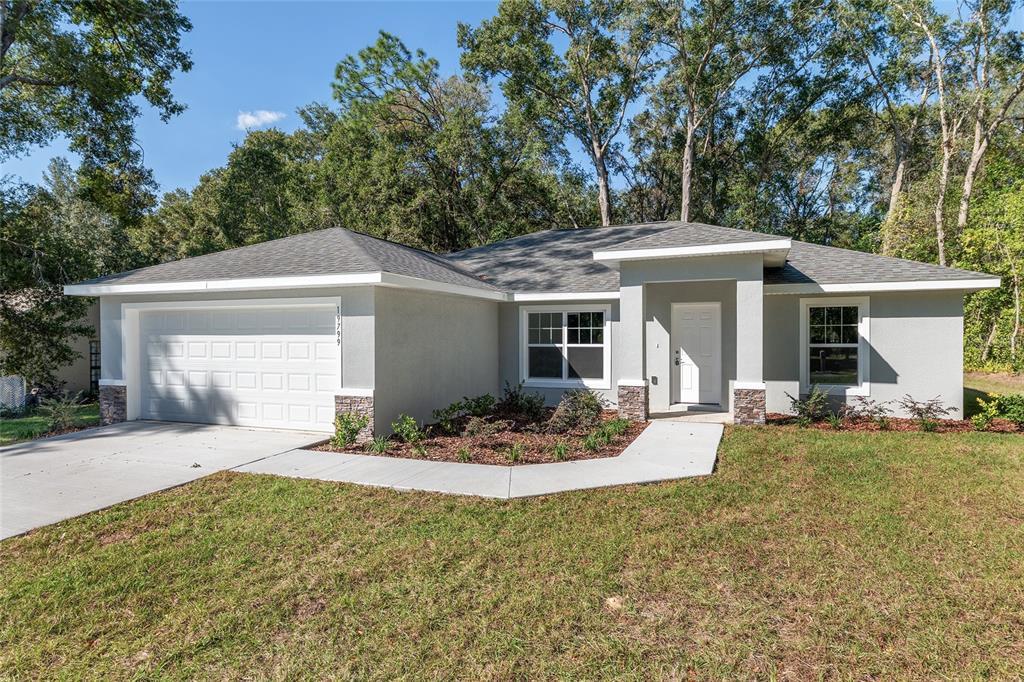 A single-story house with a gray stucco exterior, stone accents, and a two-car garage — 9776 SW 196TH CIRCLE, DUNNELLON, FL