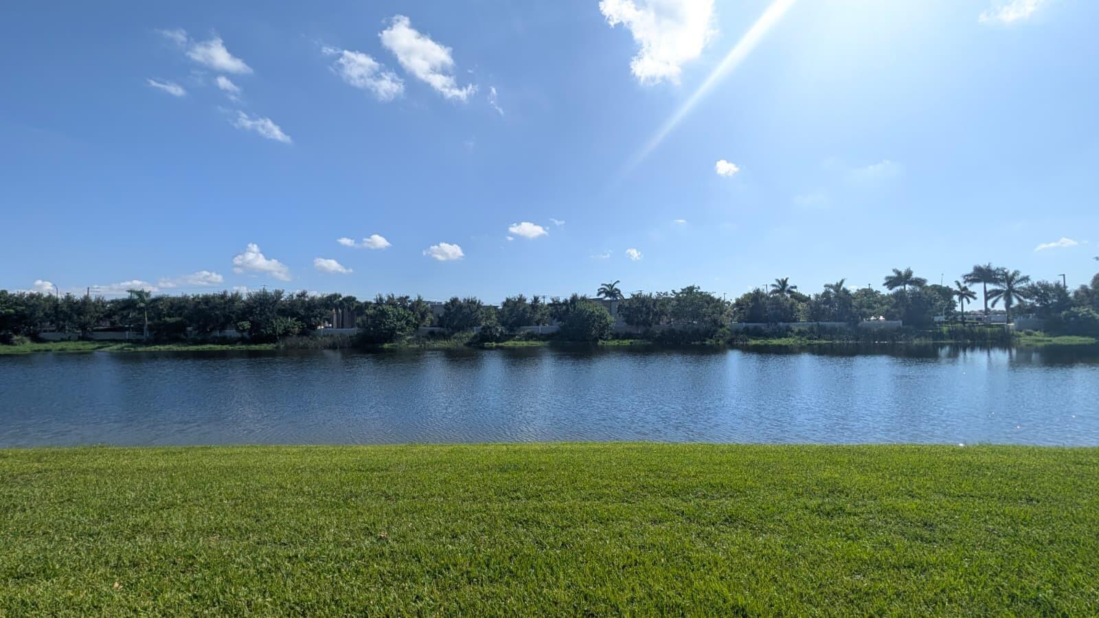 A grassy lawn overlooks a calm lake with a line of trees in the background — 4153 Cascada Circle, Cooper City FL 33024, COOPER CITY, FL