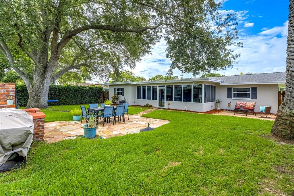 A backyard features a stone patio, outdoor dining set, and a house with a sunroom — 1636 LEISURE DRIVE, CLEARWATER, FL