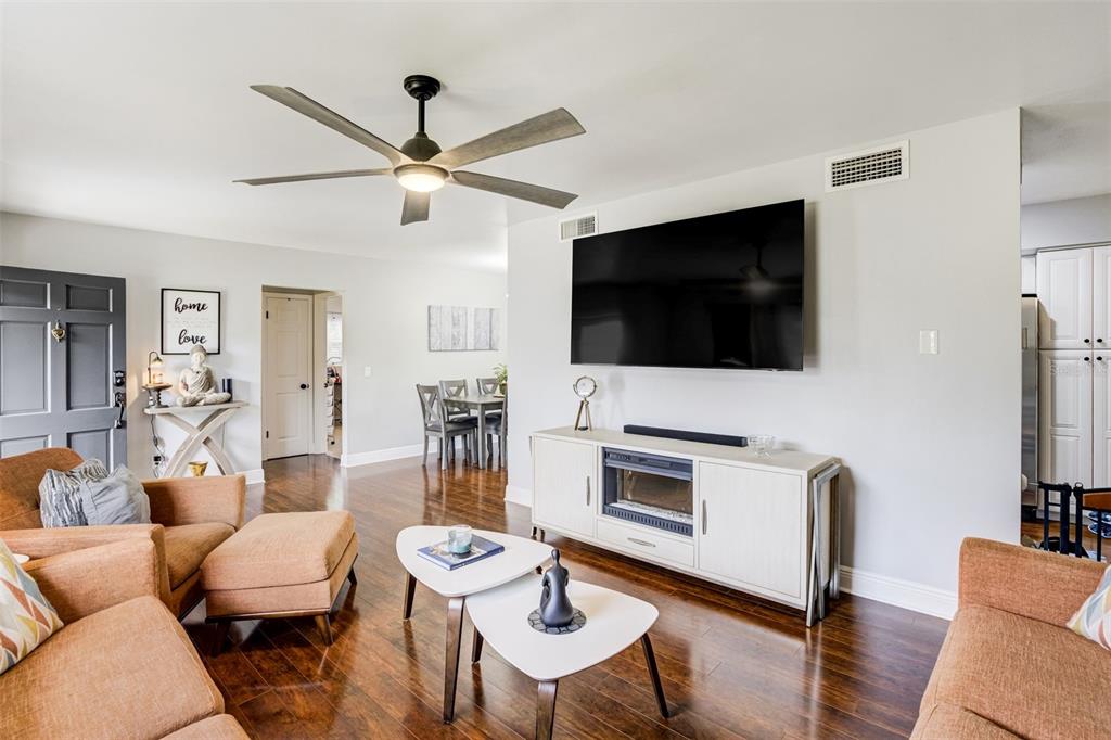 A living room features orange sofas, a television mounted above a fireplace console, and hardwood floors — 1636 LEISURE DRIVE, CLEARWATER, FL