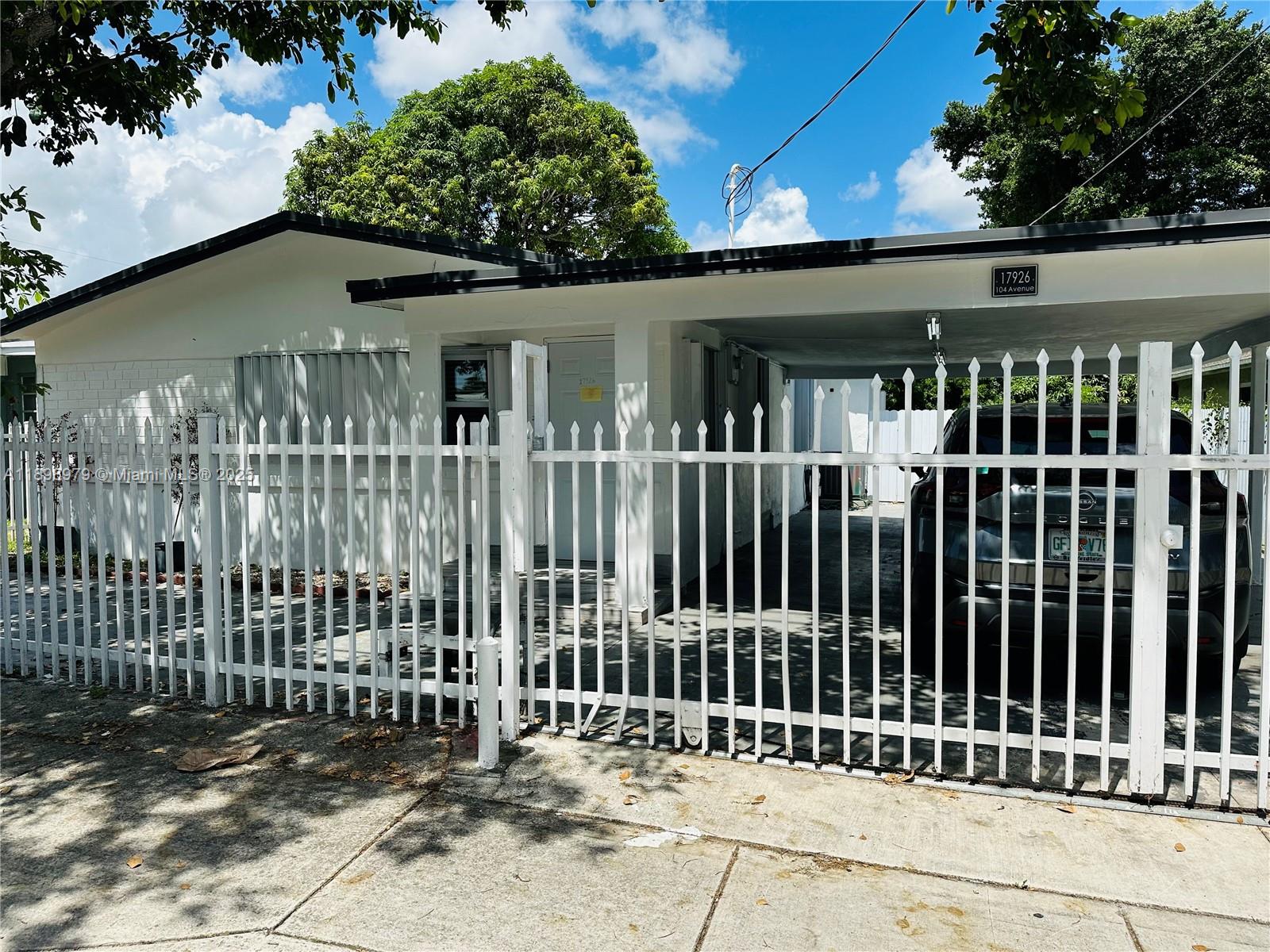 A white single-story house features a carport and a white metal picket fence — 17926 SW 104th Ave, Miami FL 33157, MIAMI, FL