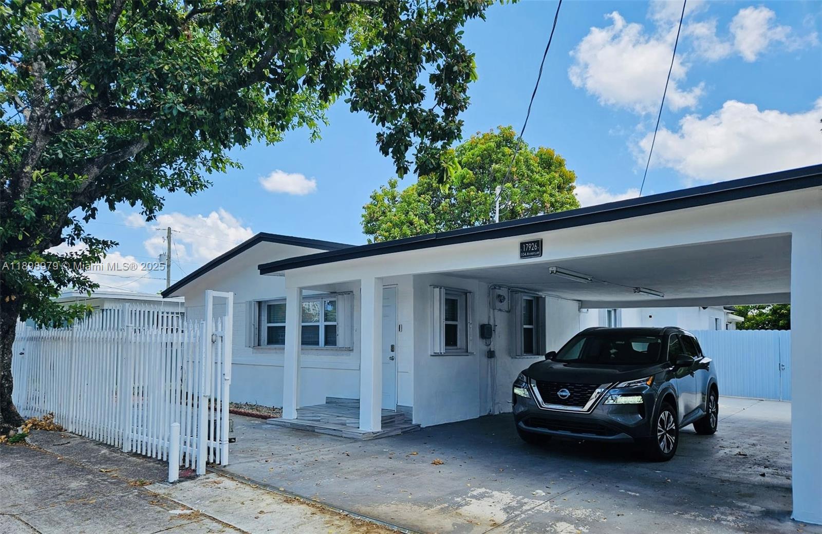 A white single-story house features a carport with a parked SUV and a white fence — 17926 SW 104th Ave, Miami FL 33157, MIAMI, FL