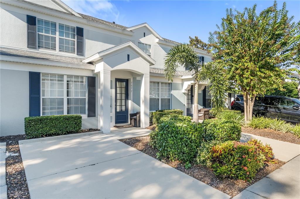 A two-story townhouse exterior features a white stucco facade, blue shutters, and a covered entryway — 7677 FITZCLARENCE STREET, KISSIMMEE, FL