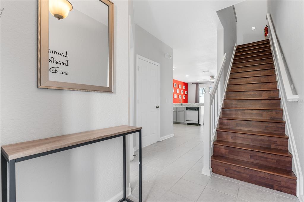 An entryway features a console table, a mirror, a staircase, and a view into a kitchen — 7677 FITZCLARENCE STREET, KISSIMMEE, FL