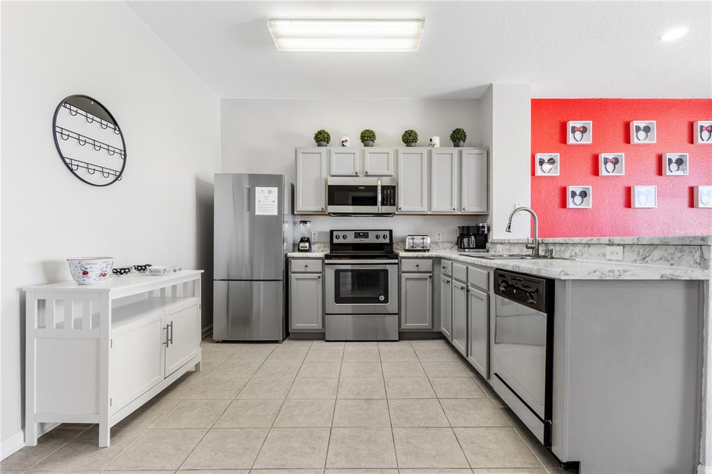 A kitchen features gray cabinets, stainless steel appliances, marble-look countertops, and a red accent wall — 7677 FITZCLARENCE STREET, KISSIMMEE, FL