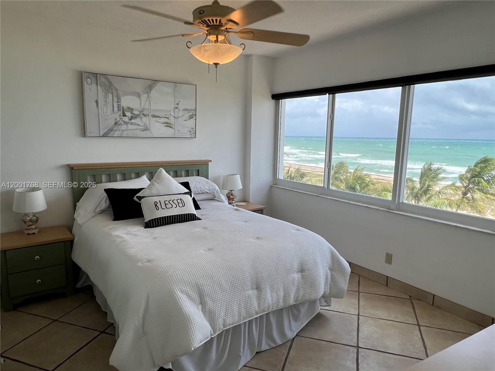 A bedroom features a bed, two nightstands, a ceiling fan, and large ocean-view windows — 710 N Ocean Blvd # 408, Pompano Beach FL 33062, POMPANO BEACH, FL