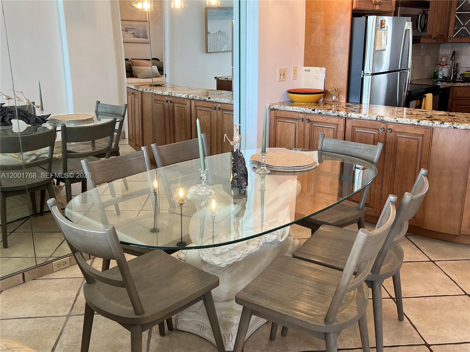 A dining area features a glass-topped table with a sculptural base and wooden chairs — 710 N Ocean Blvd # 408, Pompano Beach FL 33062, POMPANO BEACH, FL