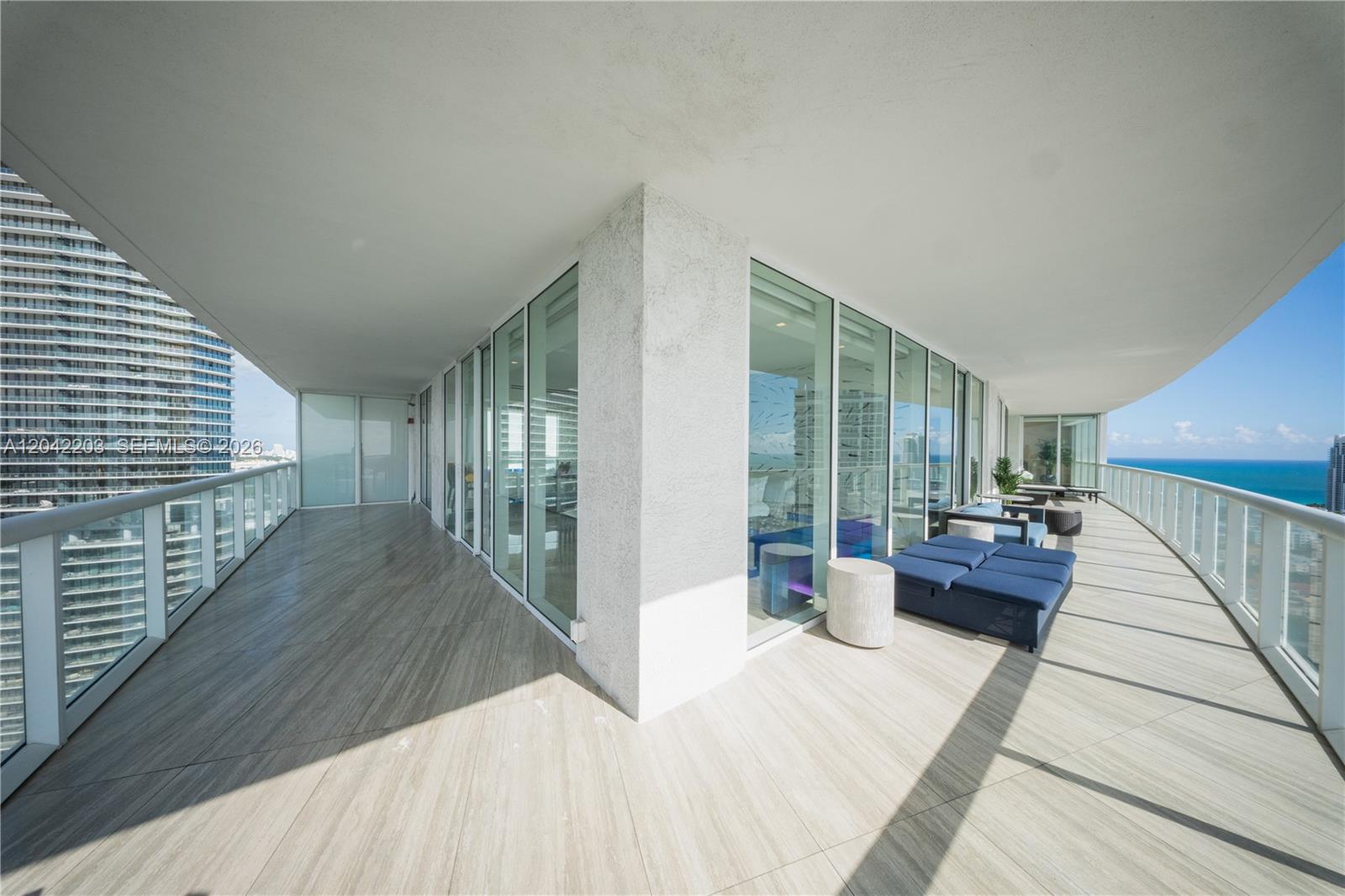 A spacious wrap-around balcony features light-colored tile flooring, glass railings, and outdoor lounge seating — 450 Alton Rd # 3301, Miami Beach FL 33139, MIAMI BEACH, FL