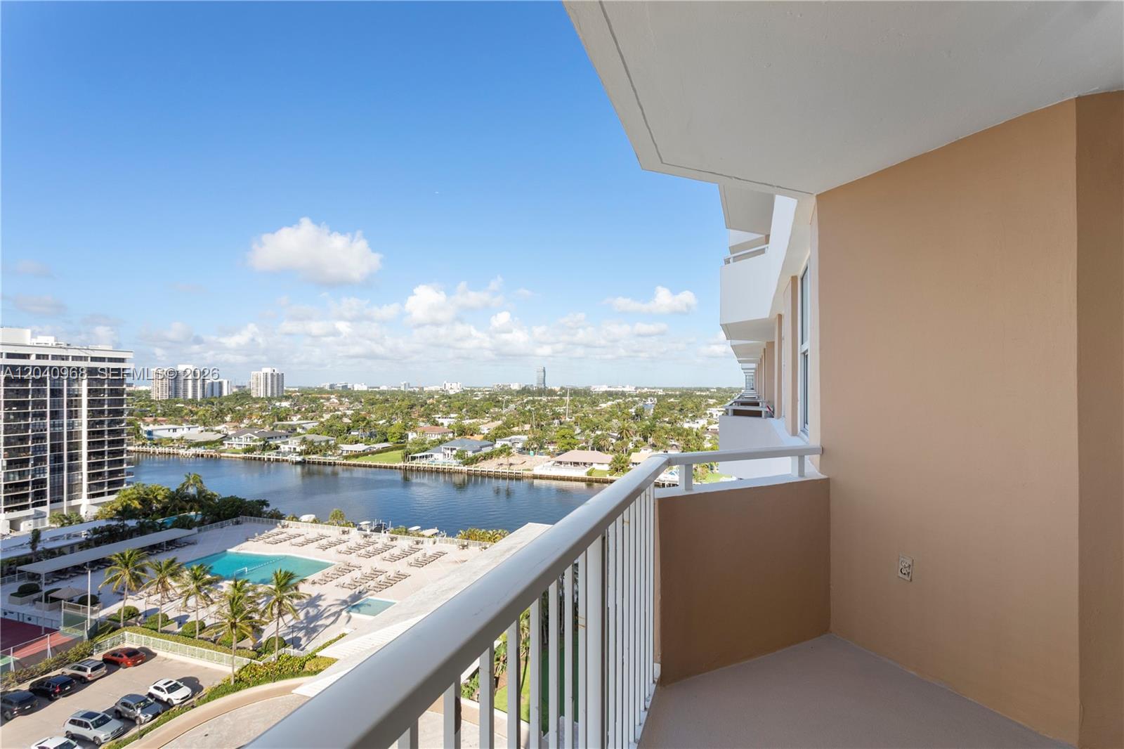 A high-rise balcony overlooks a swimming pool, a waterway, and a suburban landscape — 1965 S Ocean Dr # 11E, Hallandale Beach FL 33009, HALLANDALE BEACH, FL