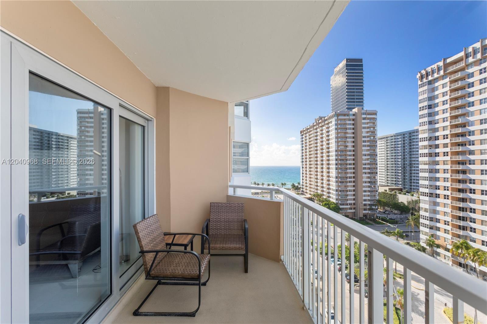 A balcony with two wicker chairs overlooks a city street and the ocean — 1965 S Ocean Dr # 11E, Hallandale Beach FL 33009, HALLANDALE BEACH, FL