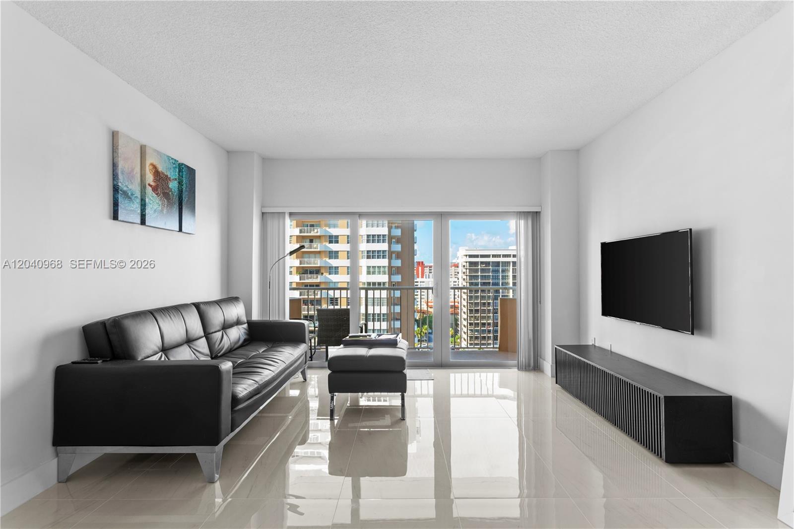 A modern living room features a black leather sofa, media console, and floor-to-ceiling windows — 1965 S Ocean Dr # 11E, Hallandale Beach FL 33009, HALLANDALE BEACH, FL