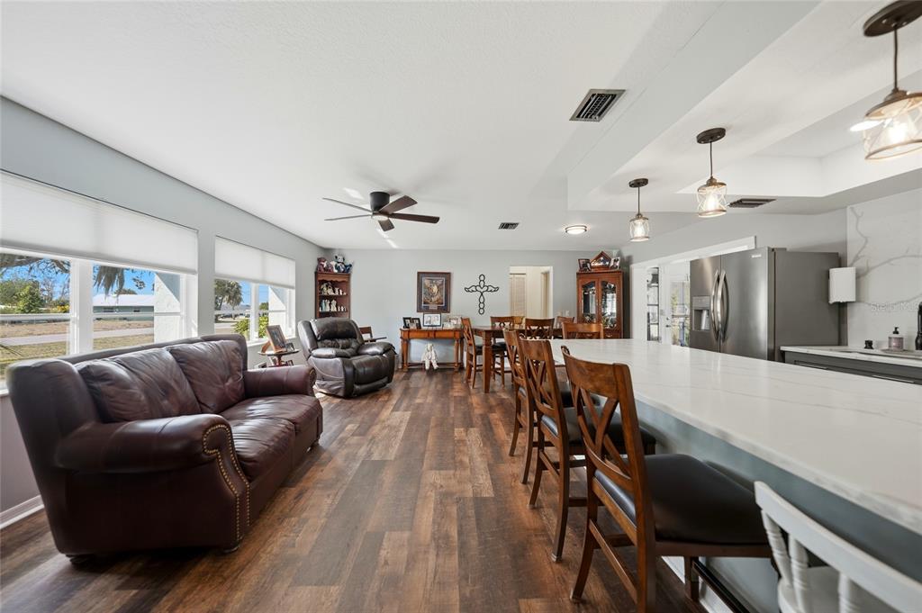 An open-concept living and kitchen area features wood-look flooring, a leather sofa, and island seating — 405 RIDGECREST DRIVE, PUNTA GORDA, FL