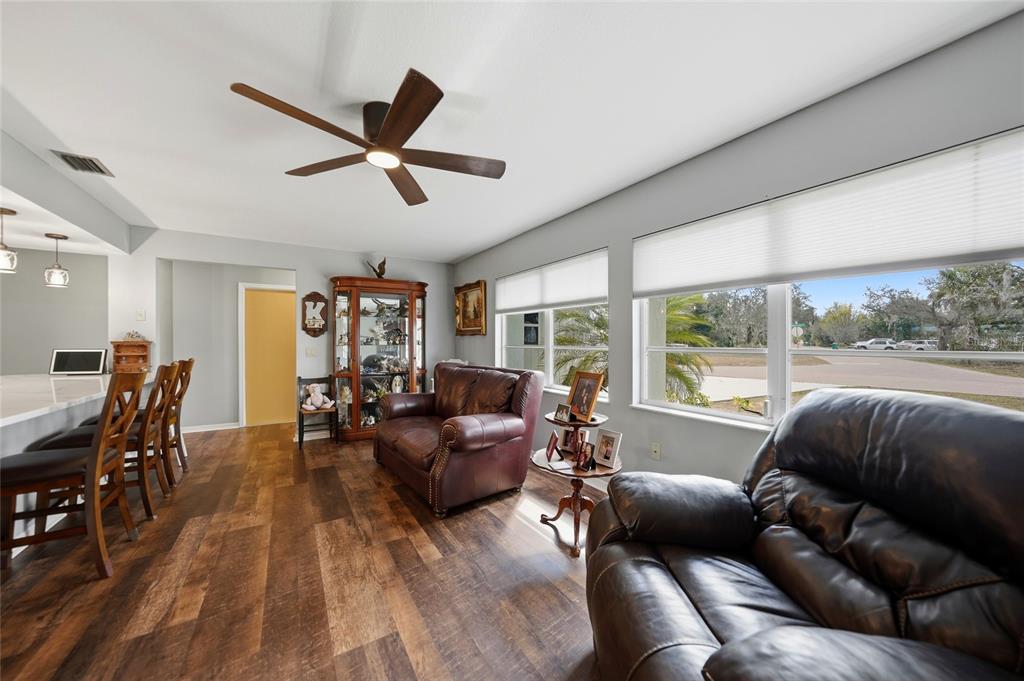 A living room features dark leather furniture, wood-look flooring, and large windows with blinds — 405 RIDGECREST DRIVE, PUNTA GORDA, FL
