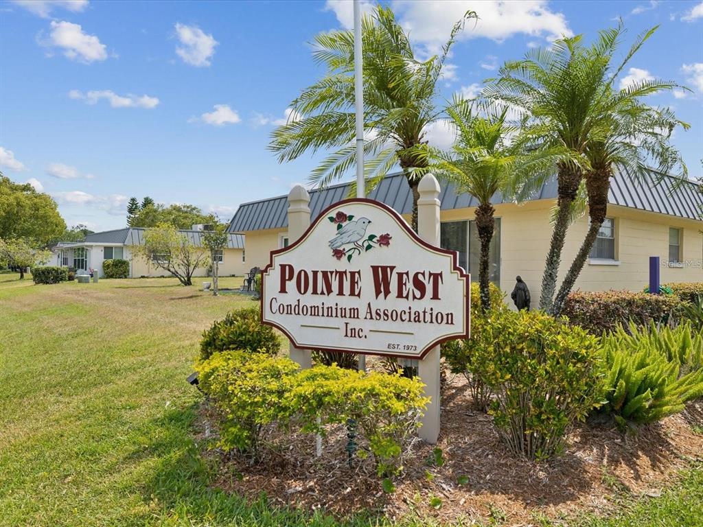 A sign for Pointe West Condominium Association stands in front of a yellow building — 11935 BAYONET LANE UNIT 0, NEW PORT RICHEY, FL