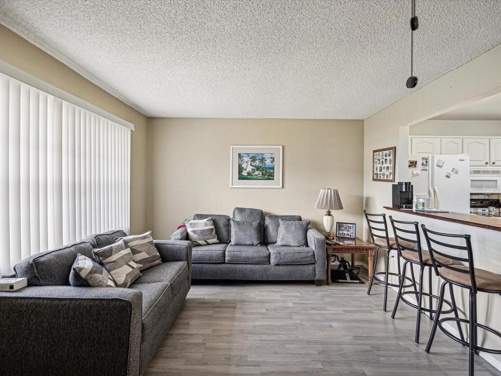 A living room with two gray sofas, wood-look flooring, and a breakfast bar with stools — 11935 BAYONET LANE UNIT 0, NEW PORT RICHEY, FL