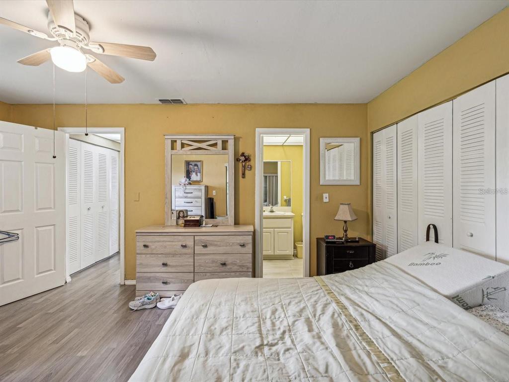 A bedroom features yellow walls, wood-look flooring, a dresser with a mirror, and white closets — 11935 BAYONET LANE UNIT 0, NEW PORT RICHEY, FL