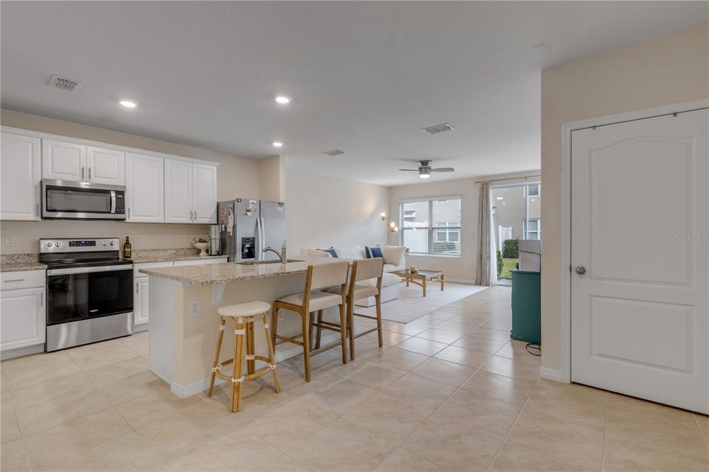 A kitchen with white cabinets and granite countertops opens into a living area with tile — 60 BELLA OAKS DRIVE, PORT ORANGE, FL