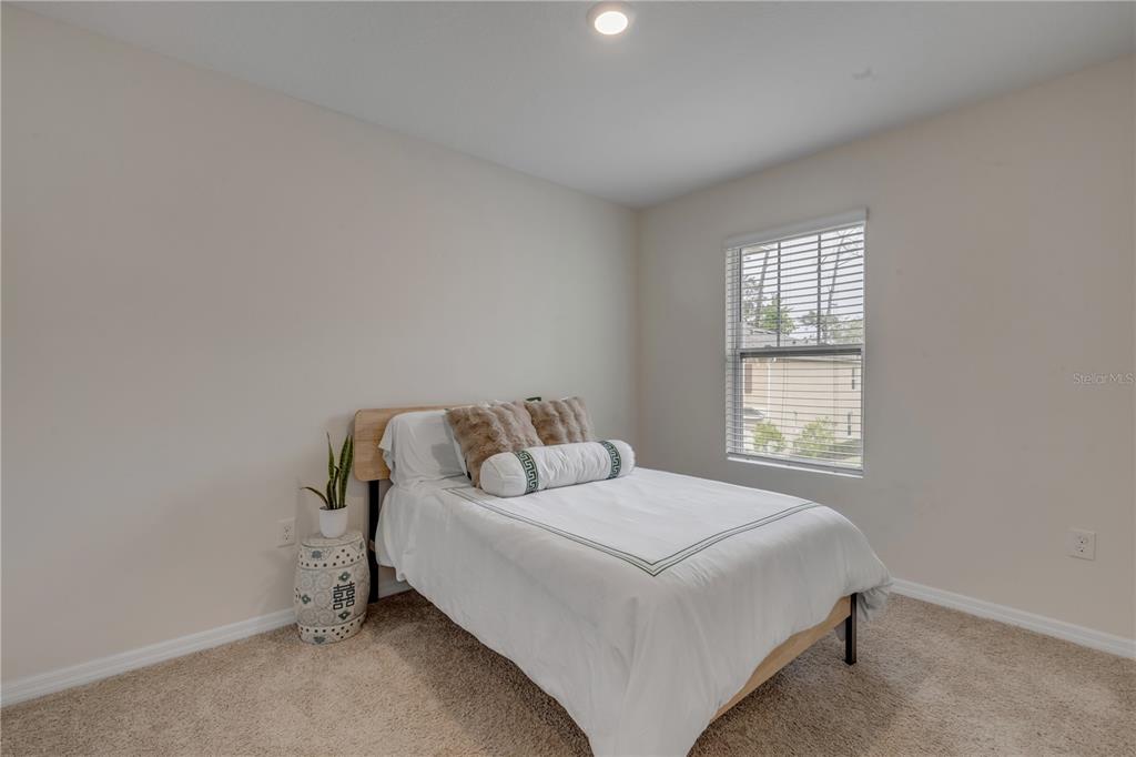 A bedroom features a bed with white bedding, a decorative side stool, and a window — 60 BELLA OAKS DRIVE, PORT ORANGE, FL