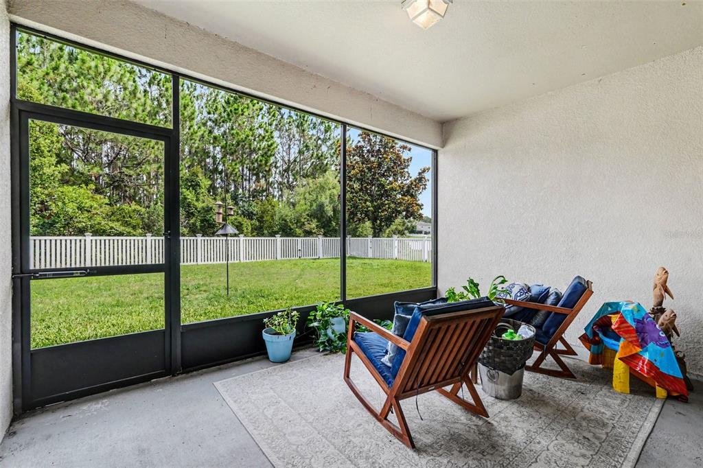 A screened-in patio features a concrete floor, two wooden chairs, and a view of a yard — 20057 OAKFLOWER AVENUE, TAMPA, FL