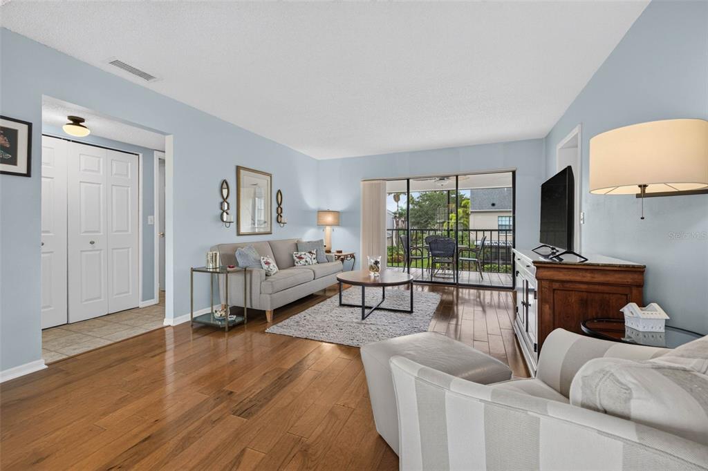 A living room features hardwood floors, a gray sofa, a coffee table, and a balcony view — 2490 HERON TERRACE UNIT #F203, CLEARWATER, FL