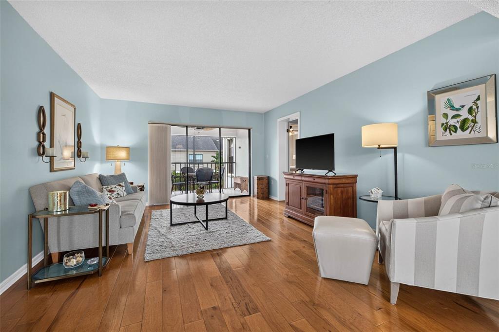 A living room with light blue walls, hardwood floors, a sofa, and a balcony view — 2490 HERON TERRACE UNIT #F203, CLEARWATER, FL