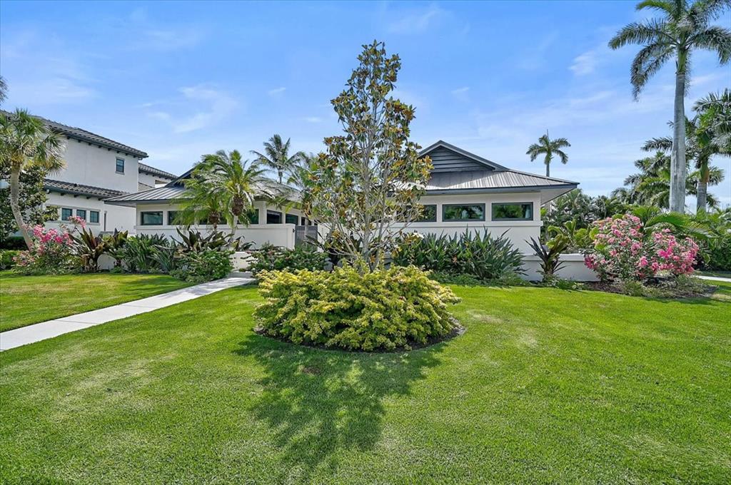 A modern house with a metal roof sits behind a landscaped lawn and palm trees — 627 OWL WAY, SARASOTA, FL