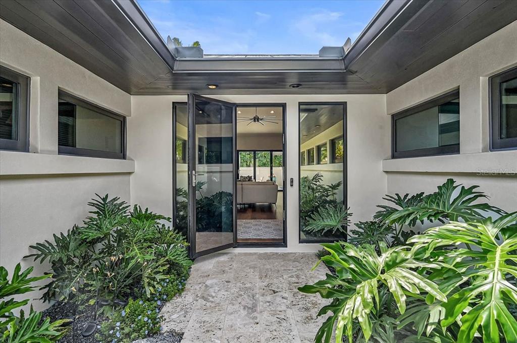 An open-air entryway features a glass door, stone flooring, and lush tropical plants — 627 OWL WAY, SARASOTA, FL