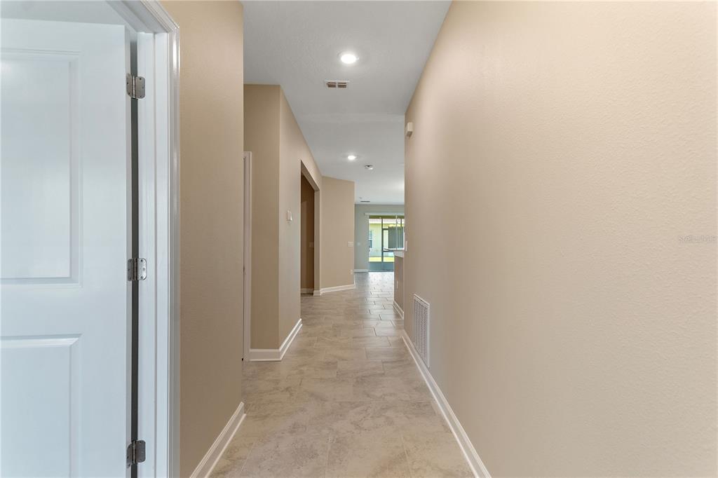 A hallway with light-colored tile flooring leads toward a bright living area with a glass door — 1064 BLACKWOLF RUN ROAD, DAVENPORT, FL