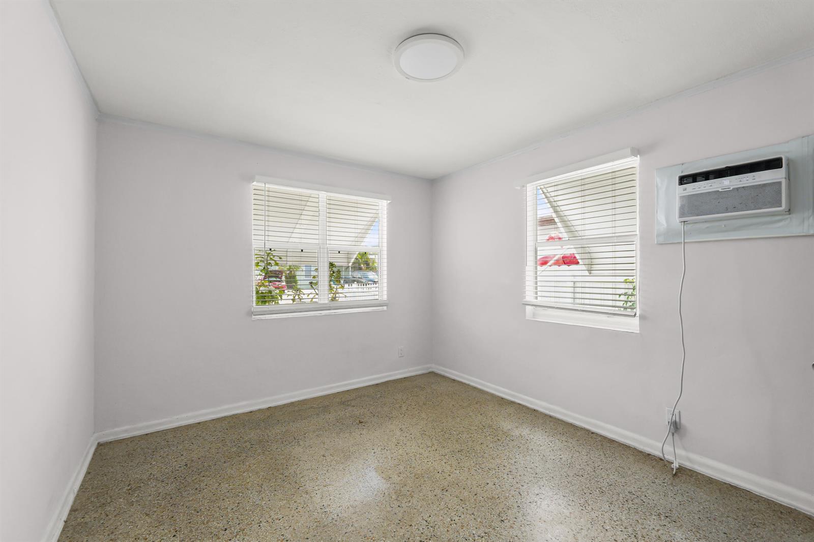 An empty bedroom with white walls, terrazzo flooring, two windows, and a window air conditioner — 429 Lytle Street, West Palm Beach FL 33405, WEST PALM BEACH, FL