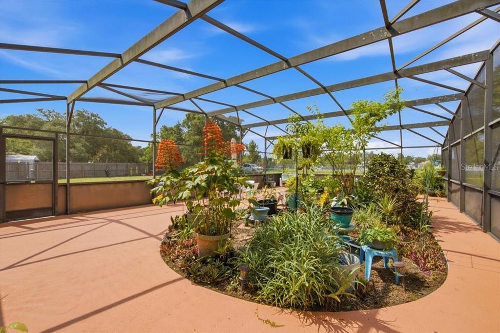 A screened-in patio features a large central garden bed filled with various potted plants — 2266 LAKE LIZZIE COURT, ST CLOUD, FL